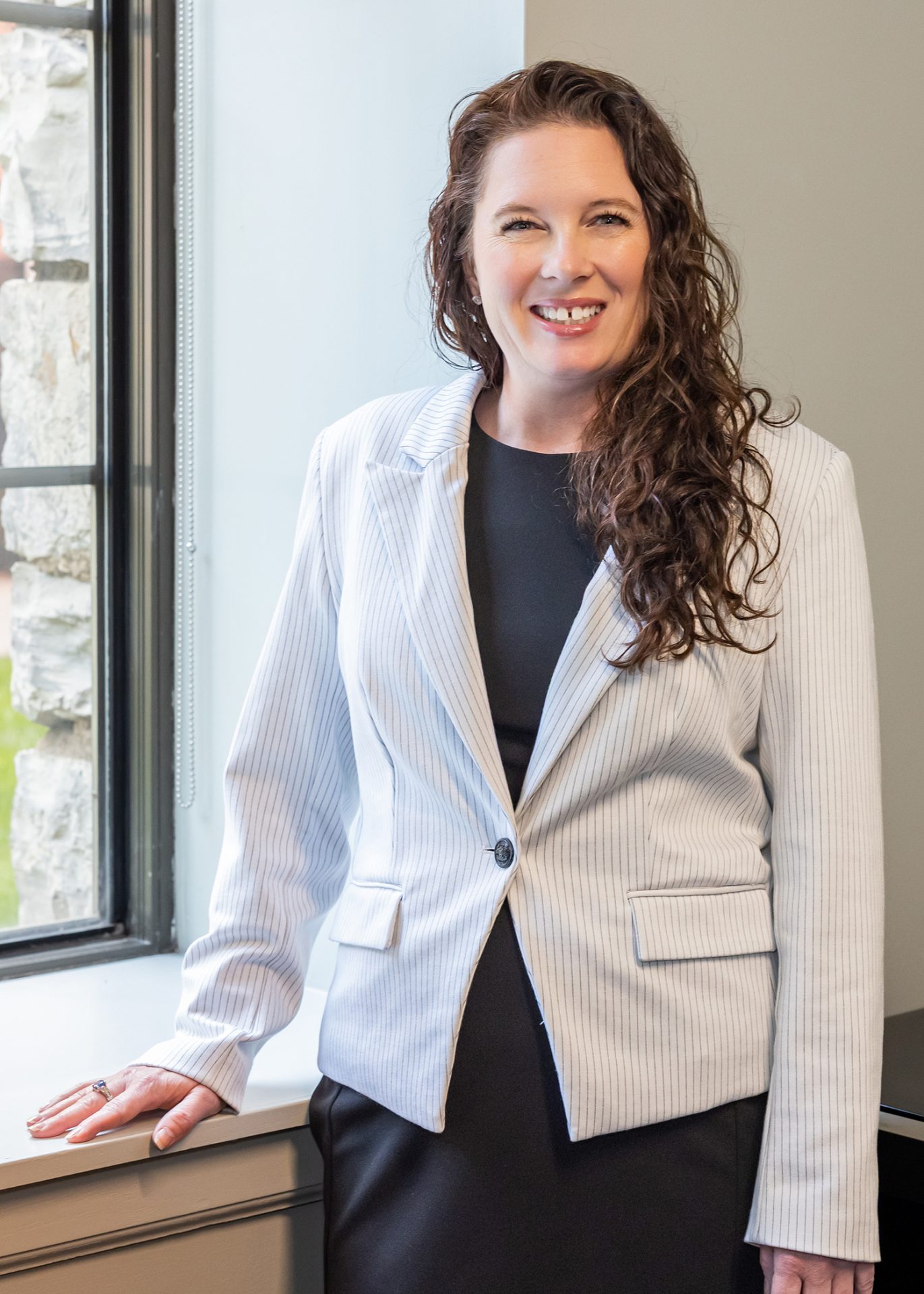 Professional portrait of a woman in a light pinstripe blazer smiling in an office setting.