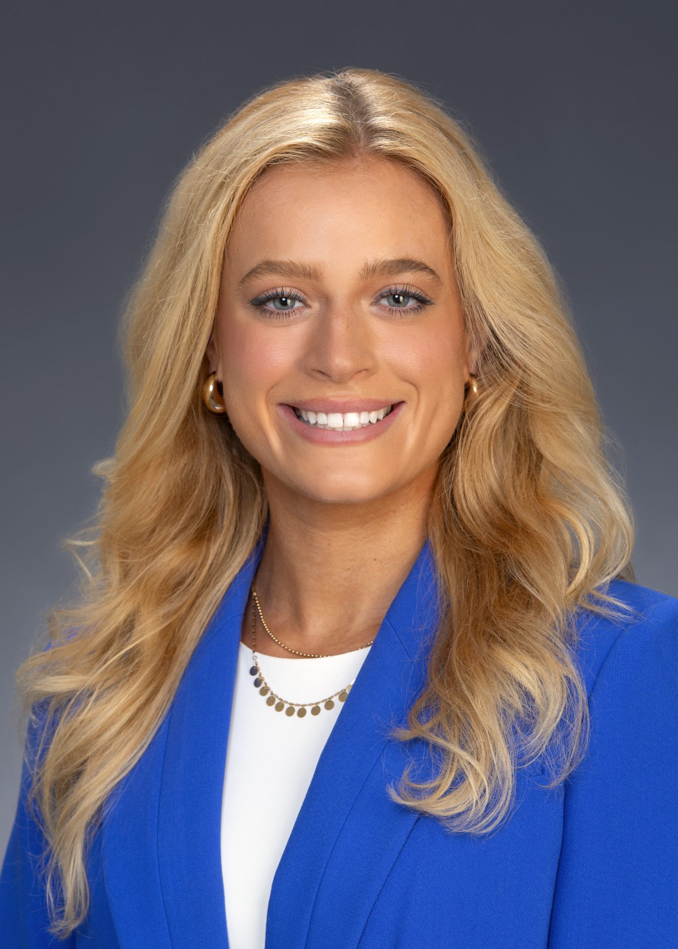 AM_McCann_5x7 Professional headshot of a woman a blue blazer, smiling against a neutral background.