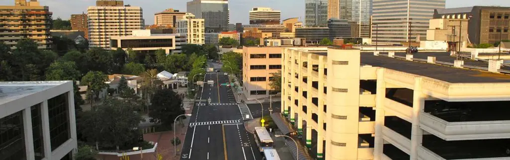 A cityscape view of White Plains, NY, featuring modern high-rise buildings and a tree-lined street at sunset.