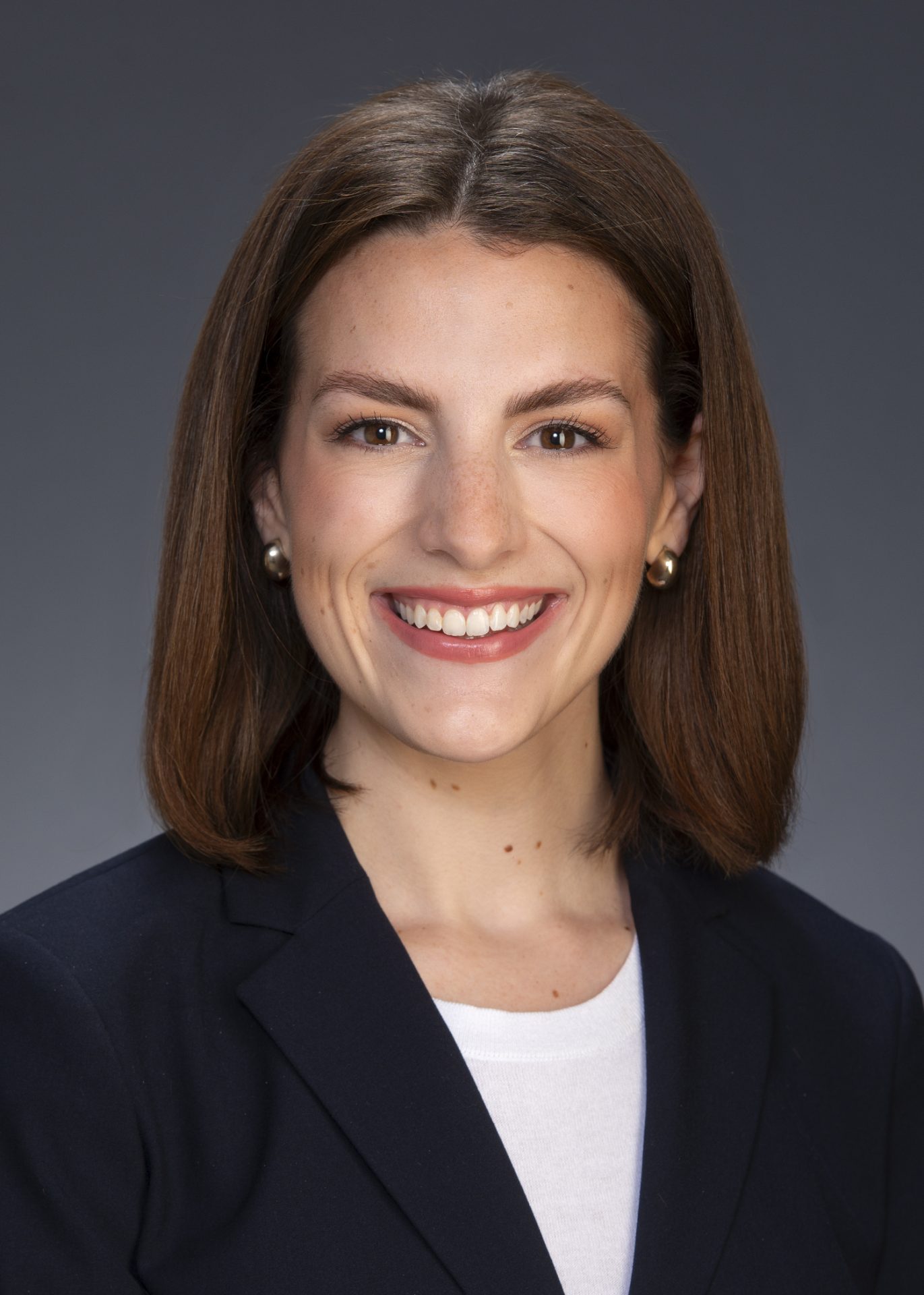 Read_Gabby_5x7 Professional headshot of a woman in a dark blazer smiling against a neutral background.