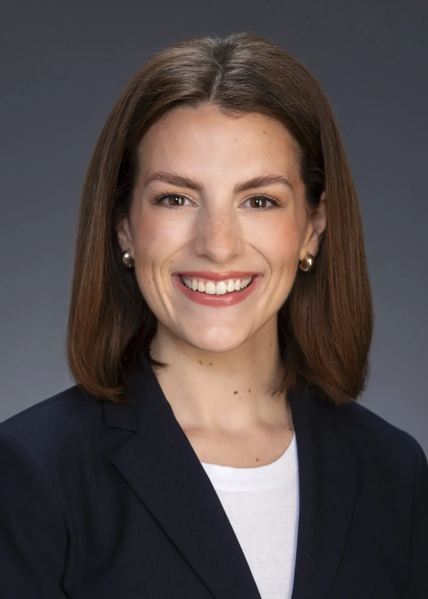 Read_Gabby_5x7 Professional headshot of a woman in a dark blazer smiling against a neutral background.
