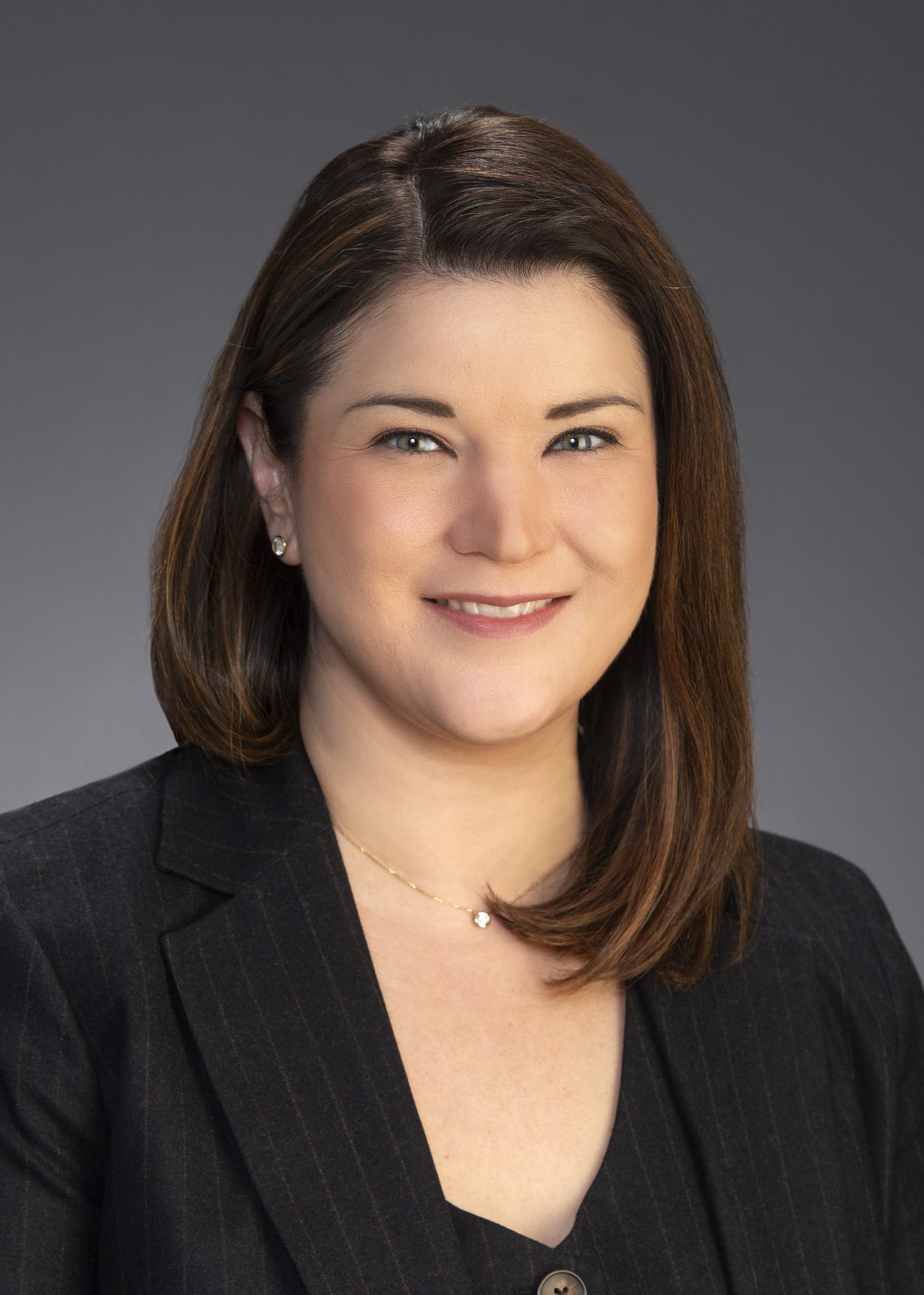 SAB_Bergman_5x7 Professional headshot of a woman in a dark blazer smiling against a neutral background.