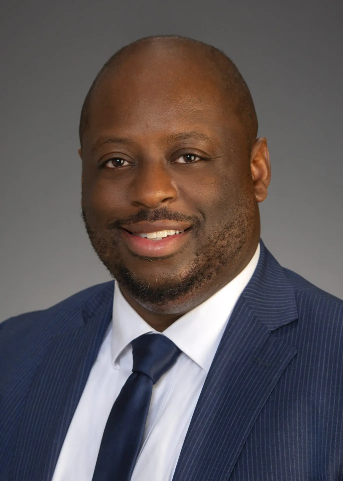 VP_Paul_5x7 Professional headshot of a man in a pinstripe suit and tie, smiling against a neutral background.